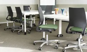 Moderna stolar med grön sits och svarta ryggstöd, placerade runt vita bord. En miljö som främjar ergonomi i skolan för bekvämt lärande.