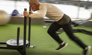 Man över 50 år som bygger muskler genom att dra en släde på ett gym.