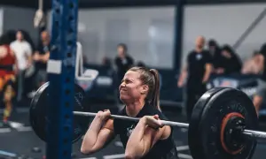 Kvinna med koncentrerat ansikte lyfter skivstång under ett crossfit pass.