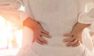 Gravid kvinna med ryggskott håller sig om ländryggen. Smärtan lyser orange.