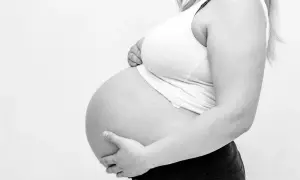 Gravid kvinna håller sin mage. Hon känner sig trött och har ont i ljumsken.