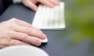 Händer som arbetar vid ett tangentbord och en mus. En person upplever en kramp i armen efter långvarigt arbete.