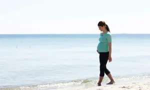 Gravid kvinna med ont i nedre delen av magen tidigt i graviditeten går längs stranden.
