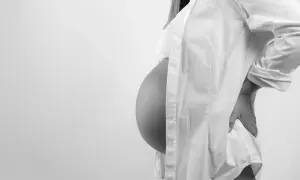 Gravid kvinna med stor mage, klädd i vit skjorta, håller handen på ryggen. En naprapat kan hjälpa vid graviditetsrelaterad smärta.