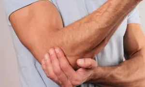En man håller sig för armbågen, som om han har ont i axel och armbåge.