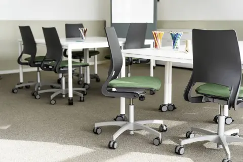 Moderna stolar med grön sits och svarta ryggstöd, placerade runt vita bord. En miljö som främjar ergonomi i skolan för bekvämt lärande.