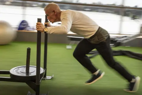 Man över 50 år som bygger muskler genom att dra en släde på ett gym.