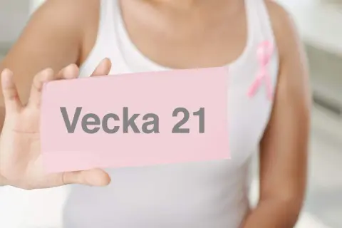 En person håller upp ett rosa kort med texten "Vecka 21". En rosa band pryder personens vita linne.