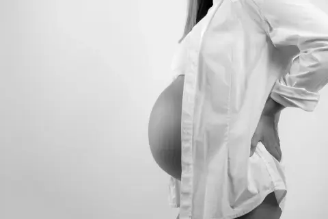 Gravid kvinna med stor mage, klädd i vit skjorta, håller handen på ryggen. En naprapat kan hjälpa vid graviditetsrelaterad smärta.
