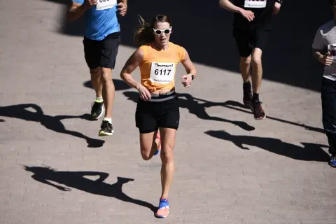 En kvinna i orange tröja och solglasögon springer i ett lopp. Hon är nummer 6117. Hur lång tid tar det att springa 5 km?