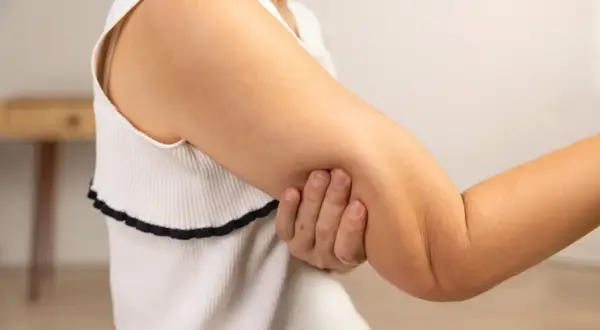 En person håller om sin armbåge, som om det gör ont i båda armarna.