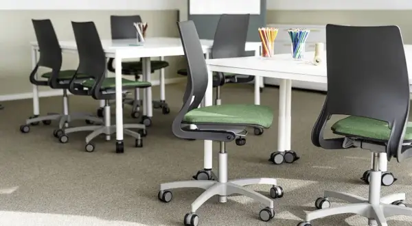 Moderna stolar med grön sits och svarta ryggstöd, placerade runt vita bord. En miljö som främjar ergonomi i skolan för bekvämt lärande.