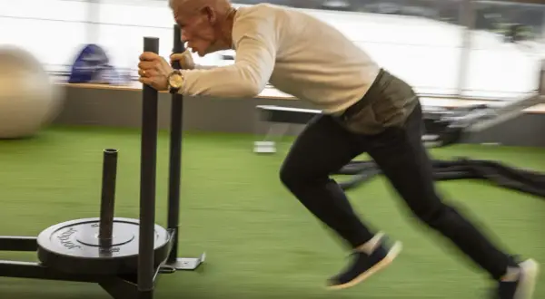 Man över 50 år som bygger muskler genom att dra en släde på ett gym.