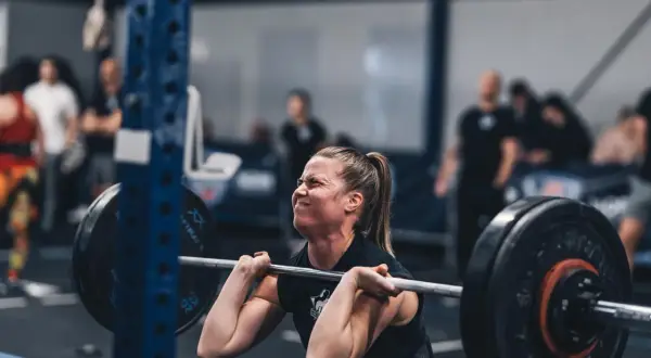 Kvinna med koncentrerat ansikte lyfter skivstång under ett crossfit pass.