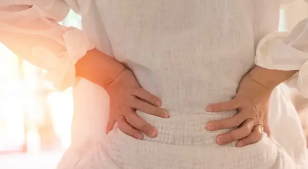 Gravid kvinna med ryggskott håller sig om ländryggen. Smärtan lyser orange.
