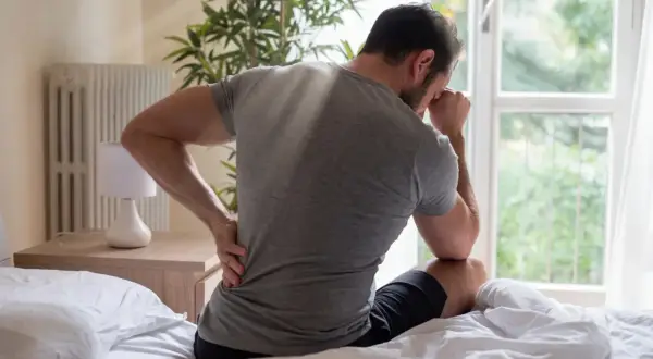 Man med ryggsmärta, håller handen mot ländryggen. Kanske dags för lite stretcha ischias?