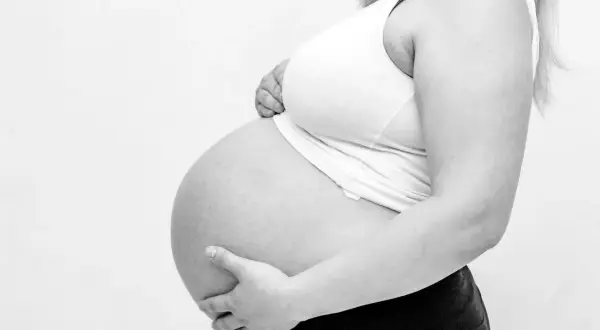 Gravid kvinna håller sin mage. Hon känner sig trött och har ont i ljumsken.