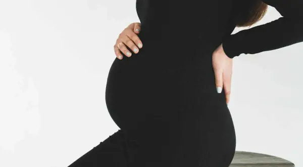 Gravid kvinna i svart klänning, med händerna på magen och ryggen. Hon kan uppleva diskbråck gravid.