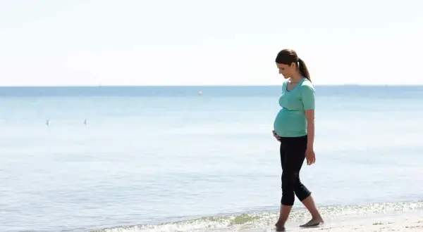Gravid kvinna med ont i nedre delen av magen tidigt i graviditeten går längs stranden.