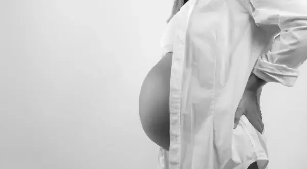 Gravid kvinna med stor mage, klädd i vit skjorta, håller handen på ryggen. En naprapat kan hjälpa vid graviditetsrelaterad smärta.