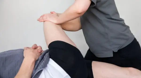 En terapeut utför en piriformis stretch på en liggande person.
