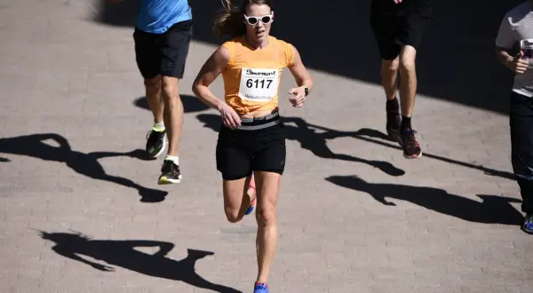 En kvinna i orange tröja och solglasögon springer i ett lopp. Hon är nummer 6117. Hur lång tid tar det att springa 5 km?