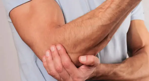 En man håller sig för armbågen, som om han har ont i axel och armbåge.