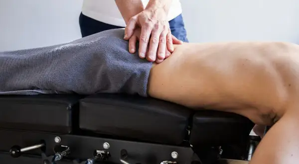 Händer som behandlar en rygg för att lindra strålar i benet. Patienten ligger på en justerbar brits.