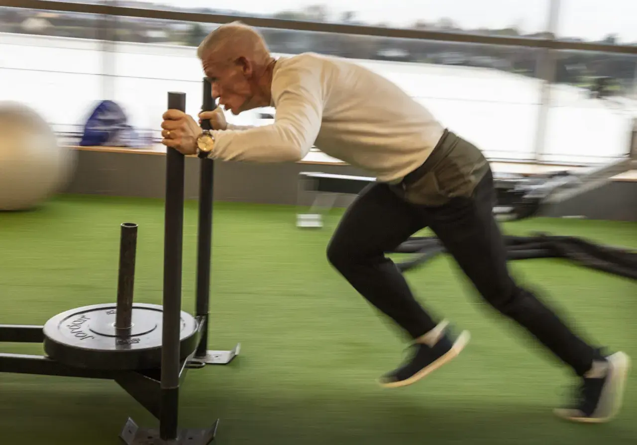 Man över 50 år som bygger muskler genom att dra en släde på ett gym.
