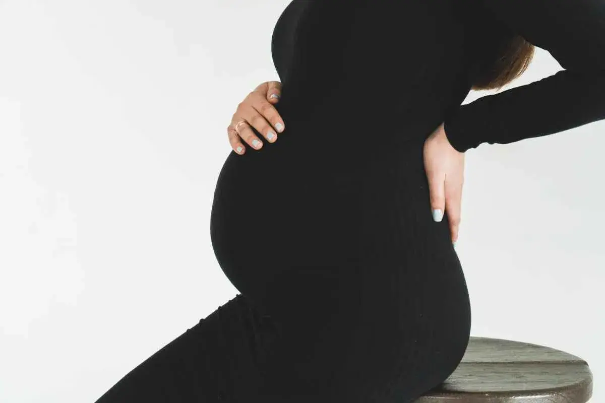 Gravid kvinna i svart klänning, med händerna på magen och ryggen. Hon kan uppleva diskbråck gravid.