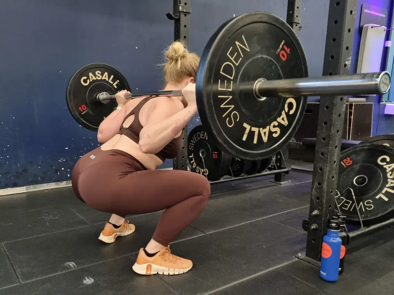 En kvinna gör squats svenska med en skivstång på axlarna i ett gym.