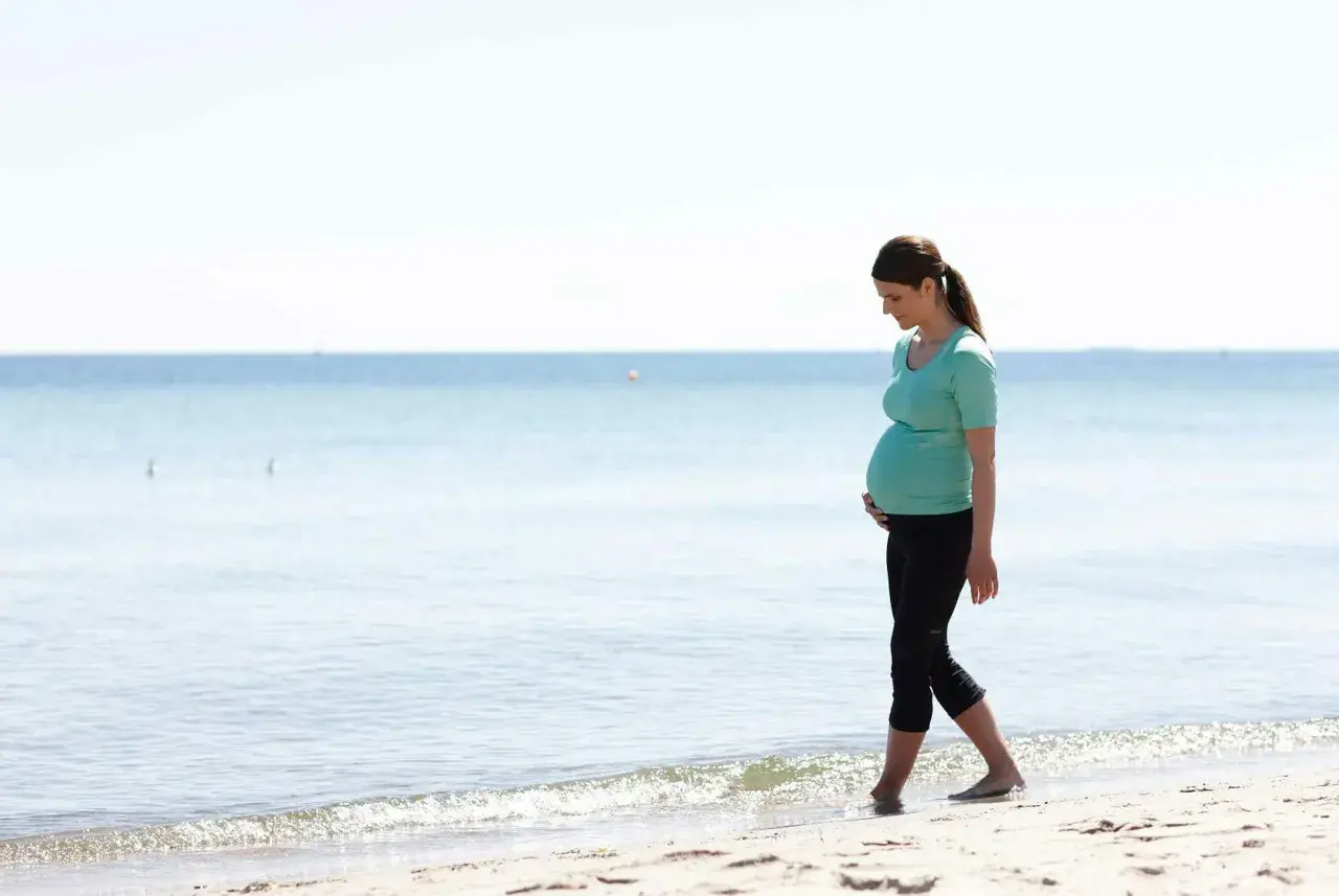 Gravid kvinna med ont i nedre delen av magen tidigt i graviditeten går längs stranden.