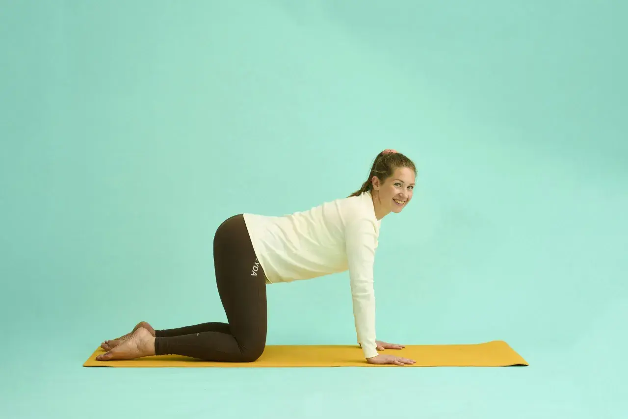 Kvinna i kattposition på yogamatta, en övning som kan lindra yoga ryggskott.