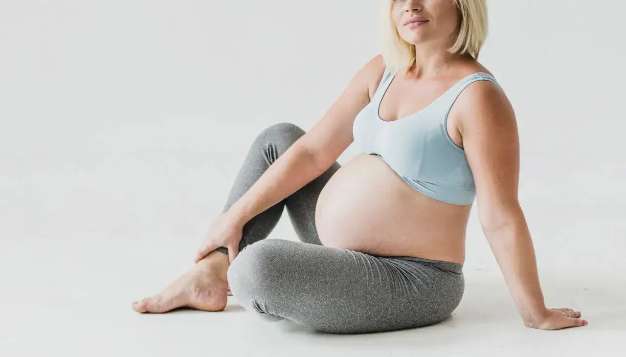 Gravid kvinna sitter p&aring; golvet, h&aring;ller om sitt ben som k&auml;nns ont.