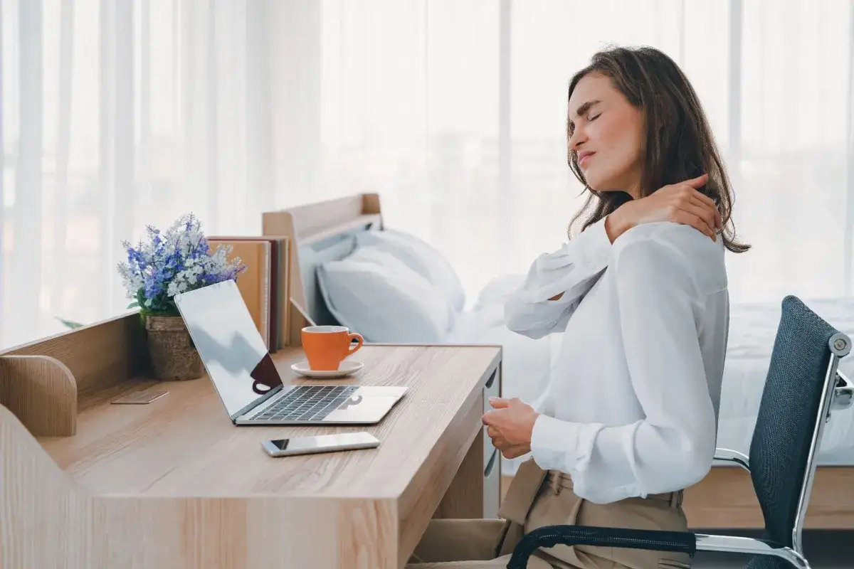 Kvinna med musarm axel som sitter vid ett skrivbord med laptop och kaffekopp.