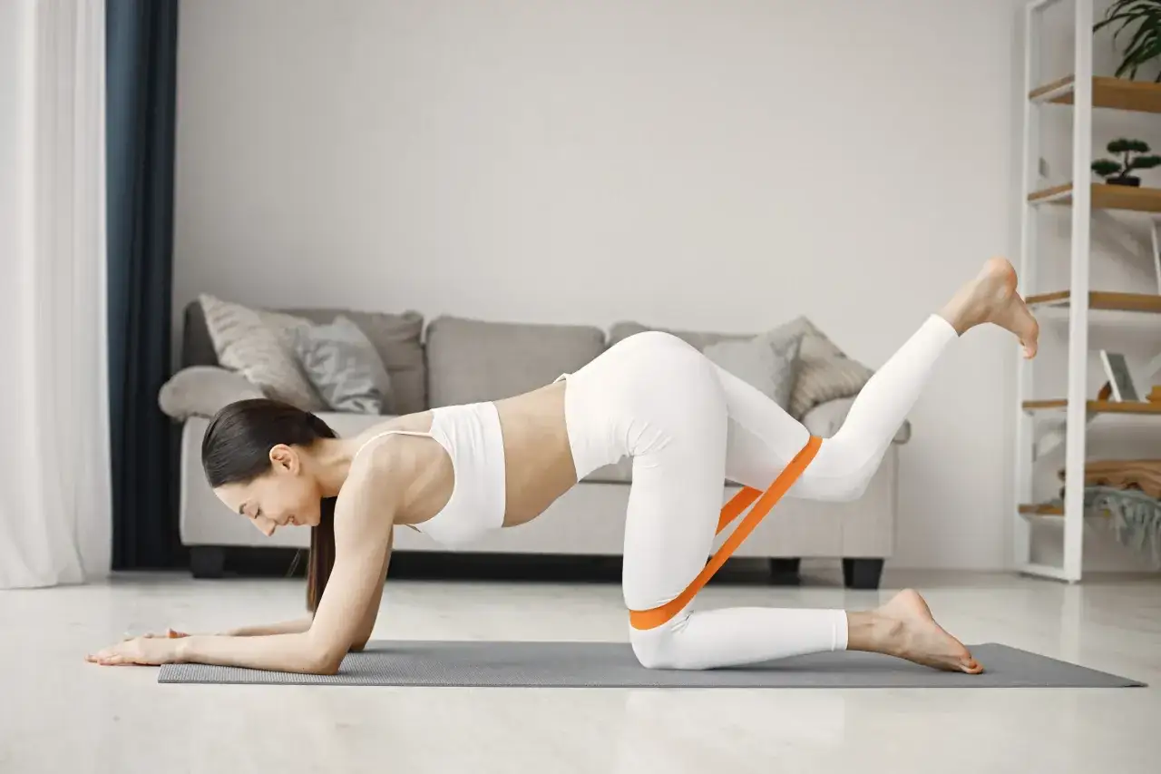 Kvinna tr&auml;nar hemma med ett orange band runt l&aring;ren f&ouml;r att st&auml;rka s&auml;tesmusklerna och lindra ont i piriformis.