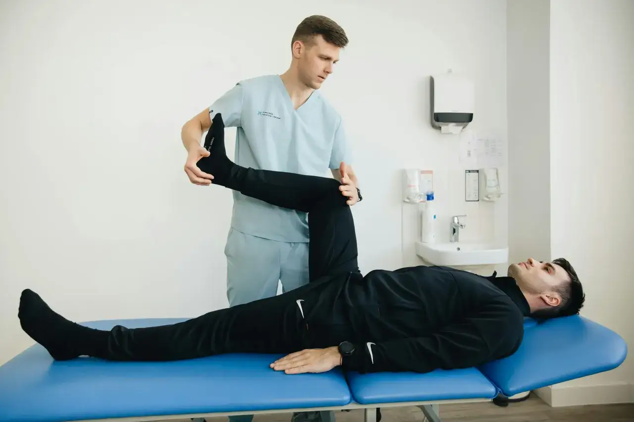 Fysioterapeut hjälper patient att stretcha ischias. Patienten ligger på en blå brits medan fysioterapeuten lyfter patientens ben.