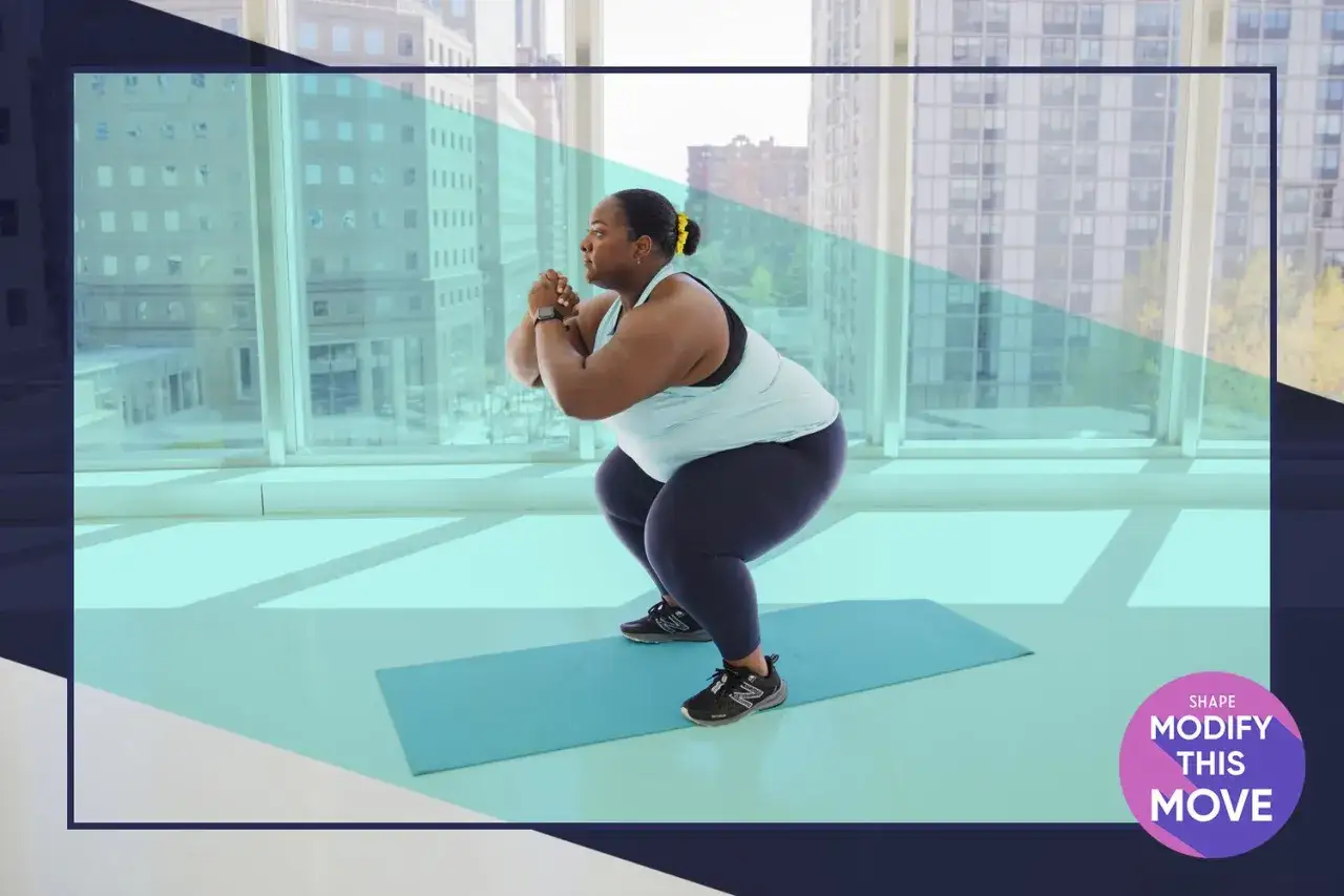 En kvinna utf&ouml;r squats svenska p&aring; en yogamatta framf&ouml;r stora f&ouml;nster.