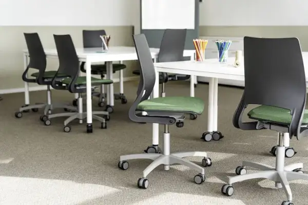 Moderna stolar med grön sits och svarta ryggstöd, placerade runt vita bord. En miljö som främjar ergonomi i skolan för bekvämt lärande.