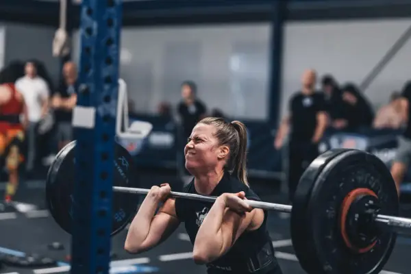 Kvinna med koncentrerat ansikte lyfter skivstång under ett crossfit pass.