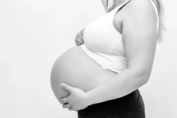 Gravid kvinna håller sin mage. Hon känner sig trött och har ont i ljumsken.