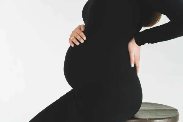 Gravid kvinna i svart klänning, med händerna på magen och ryggen. Hon kan uppleva diskbråck gravid.