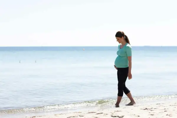 Gravid kvinna med ont i nedre delen av magen tidigt i graviditeten går längs stranden.