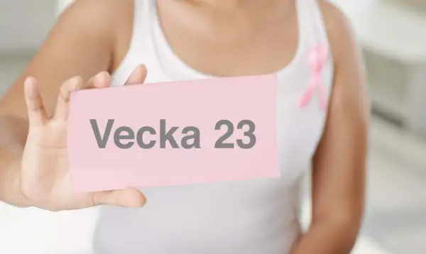 En person håller upp en rosa lapp med texten "Vecka 23". En rosa band pryder personens vita topp.