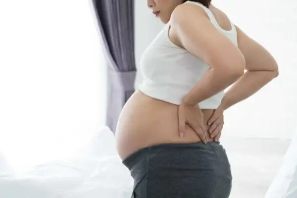 Gravid kvinna med ont i blygdbenet, håller sig om ryggen.