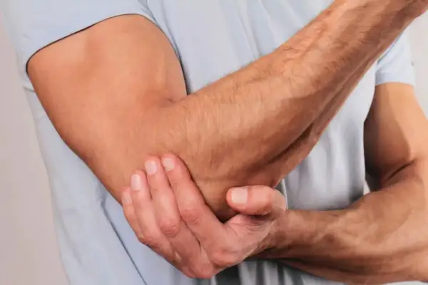 En man håller sig för armbågen, som om han har ont i axel och armbåge.