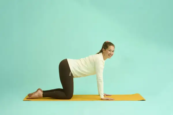 Kvinna i kattposition på yogamatta, en övning som kan lindra yoga ryggskott.
