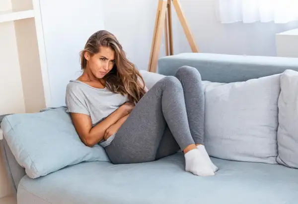 Gravid kvinna med ont i ligamenten sitter på en soffa och håller sig om magen.